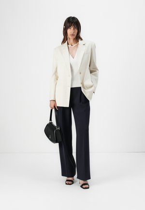Beige skreddertilpasset blazer med to knapper, hvit v-hals topp, marineblå vide bukser, svart håndveske og svarte hæler.