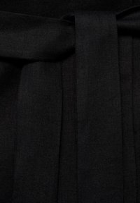 Tessuto nero con finitura testurizzata, caratterizzato da pieghe laterali e un dettaglio a fiocco, che trasmette un design strutturato.