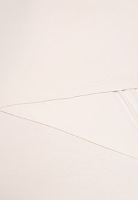 Peça de vestu�ário em bege claro, feita de um tecido suave e elástico. Possui um design assimétrico com seções em camadas e costuras limpas e discretas.