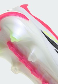 Κοντινό πλάνο της σόλας ενός λευκού και ροζ ποδοσφαιρικού παπουτσιού με διαφανείς τάπες και εμφανές το κείμενο "POWERSPINE" και "PREDATOR".