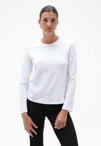Biała koszula z długim rękawem, wykonana z miękkiego materiału, z klasycznym okrągłym dekoltem, w zestawie z czarnymi prążkowanymi spodniami. Prosty, funkcjonalny design.