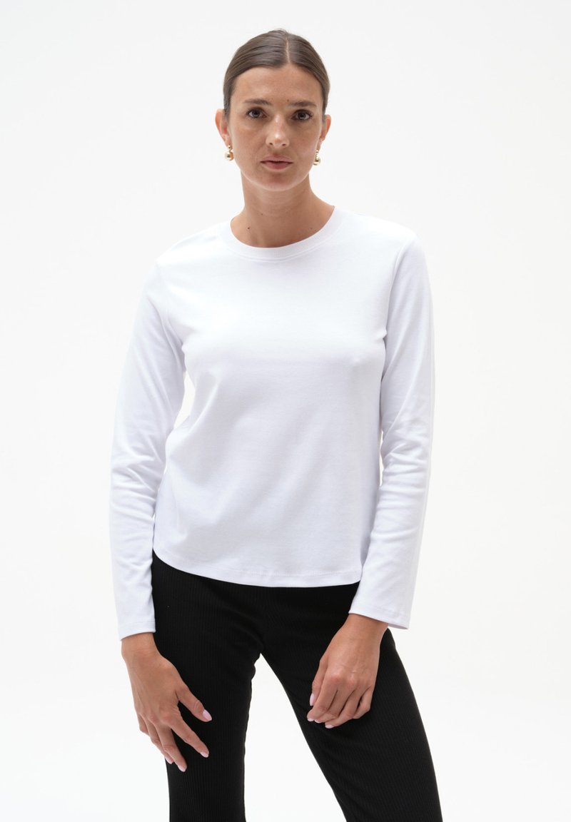 Biała koszula z długim rękawem, wykonana z miękkiego materiału, z klasycznym okrągłym dekoltem, w zestawie z czarnymi prążkowanymi spodniami. Prosty, funkcjonalny design.