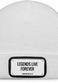 Balta megzta kepurė su užlenktu kraštu. Atrodo su juodu stačiakampiu paženklintojimu, kuriame užrašyta "LEGENDS LIVE FOREVER" ir prekės ženklas po juo.