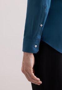 Teal langef sleeveshirt met een gladde textuur, voorzien van ronde manchetten en witte knopen. Borduursel op de manchetten is zichtbaar.