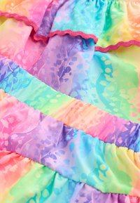 Flerfärgat chiffongtyg med volanglager i pastellnyanser av rosa, lila, blått och grönt, med ett subtilt blommönster och vågig kant.