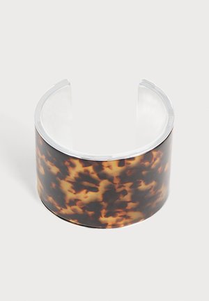 Large bracelet manchette ouvert avec motif écaille marron et noir et bords argentés sur fond uni.
