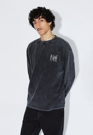 Mørkegrå langærmet sweatshirt lavet af blødt stof med et hvidt grafisk motiv på fronten. Rund hals og afslappet pasform.