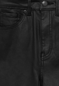 Gros plan sur un pantalon en cuir noir montrant la poche avant, les passants de ceinture, les coutures et le bouton avec le détail du nom de la marque.