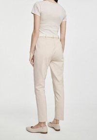 Beżowe spodnie dopasowane, charakteryzujące się gładką fakturą i tylnymi kieszeniami. Połączone z jasnymi butami dla uzyskania spójnego wyglądu.