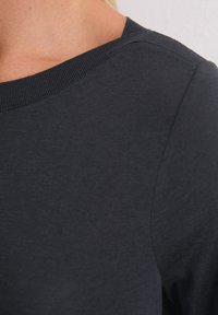 Donkergrijze longsleeve kleding met een gladde textuur, voorzien van een ronde halslijn en geribde manchetten. Subtiele glans zonder zichtbare patronen.
