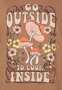 Brunt tyg har en lekfull grafik med orange och rosa svampar, blommönster och texten "GÅ UT FÖR ATT KOLLA INUTI."