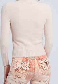 Jasnoróżowy, teksturowany sweter z wysokim kołnierzem i prążkowanym wykończeniem; noszony z wzorzystymi, kolorowymi dżinsami z kwiatowymi i zwierzęcymi nadrukami.