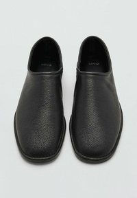 Zapatillas negras sin cordones con un acabado de piel texturizada, punta redondeada y diseño minimalista. Interior suave y suela plana.