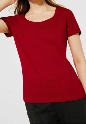 T-shirt rouge à manches courtes avec un décolleté rond, fabriqué en tissu doux et lisse, présentant une coupe ajustée et des détails de couture minimalistes.