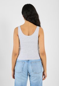 Grå ribbet tanktop med u-cut bak, parret med lyseblå høyhals jeans. Stoffet virker mykt, med en tettsittende silhuett.