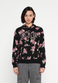 Czarna bluza z kapturem w kwiatowy wzór, z widocznym logo "GAP" w wyrazistych różowych literach. Zaprojektowana z kapturem na sznurek i ściągaczami na mankietach.