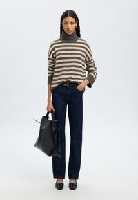 Gestreifter Rollkragenpullover in Beige und Dunkelgrau, kombiniert mit dunkelblauen, geraden Jeans. Das Model hält eine schwarze Leder-Handtasche.