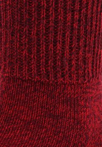 Calcetines rojos de punto con un diseño acanalado, que presentan un acabado texturizado y patrones variados en el hilo. La tela parece suave y cálida.