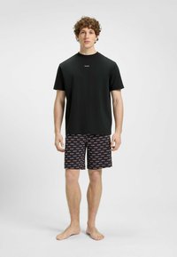 T-shirt noir à manches courtes avec le logo "HUGO" sur la poitrine, associé à un short noir présentant un motif répétitif de texte "HUGO" en rouge et blanc.