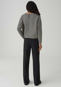 Maglione a righe bianche e nere con vestibilità morbida e maniche lunghe, con apertura a goccia sulla schiena, abbinato a pantaloni neri a gamba dritta.