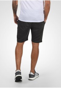Shorts de sport gris avec une coupe décontractée, associés à des baskets noires et blanches avec trois rayures et une semelle texturée.