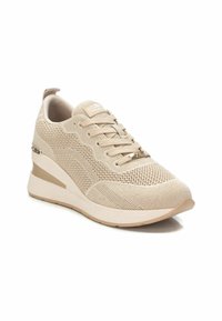 Zapatilla deportiva beige con parte superior de malla, cierre de cordones, suela acolchada y sutiles acentos metálicos en el talón; diseño en cuña para mayor altura.