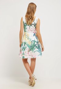 Robe à motif floral avec un corsage ajusté et une jupe évasée. Fond blanc orné de fleurs roses et vertes, avec un dos en V et un design sans manches.