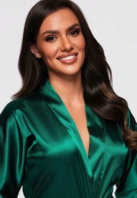 Donna sorridente con lunghi capelli scuri che indossa un accappatoio satinato verde lucido su uno sfondo chiaro e semplice.