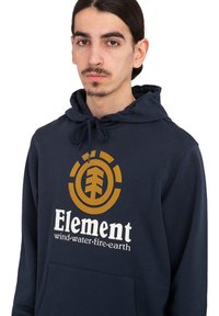 Dunkelblauer Hoodie aus Baumwolle mit einer Vorderentasche. Auf der Vorderseite befindet sich ein großes goldenes Logo und der Text "Element Wind-Wasser-Feuer-Erde".