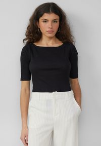 Czarny prążkowany top z krótkim rękawem i szerokim dekoltem, w zestawieniu z białymi spodniami w prążki. Gładka faktura i dopasowany krój.