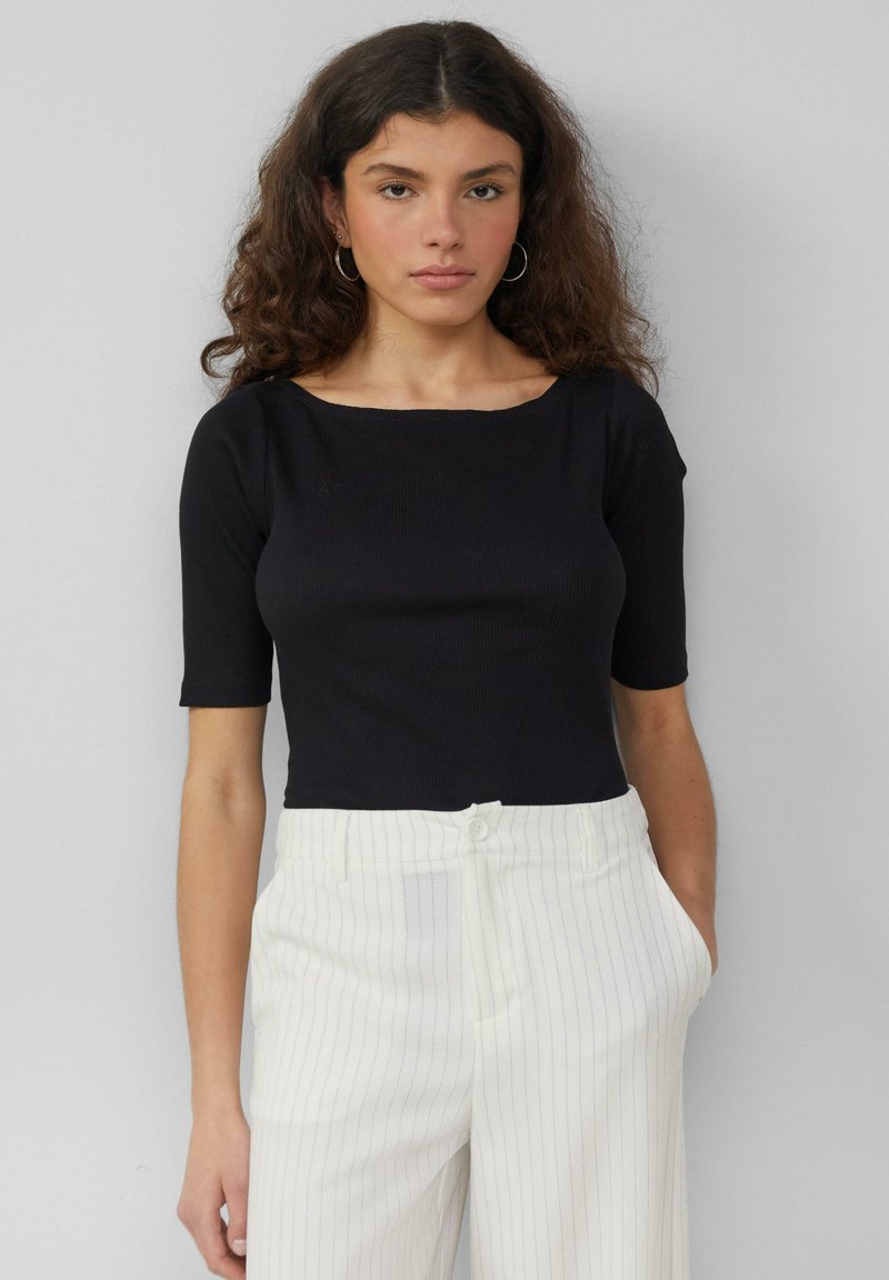 Czarny prążkowany top z krótkim rękawem i szerokim dekoltem, w zestawieniu z białymi spodniami w prążki. Gładka faktura i dopasowany krój.