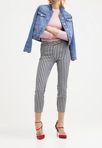 Denim jacket with a fitted design, light blue color, two chest pockets. Light pink ribbed sweater, black and white checked ankle pants, red heels.