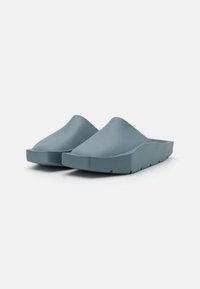Scarpe slip-on moldato in blu chiaro, con una texture liscia, design ampio e aperto, e suola spessa con scanalature per migliorare la presa.