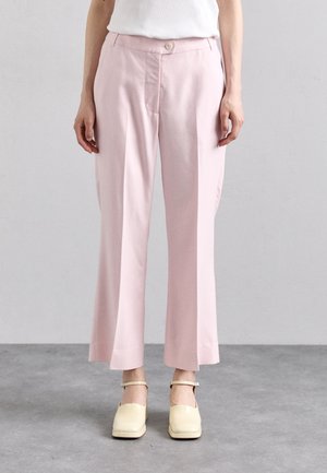 Personne portant un pantalon court rose clair avec un bouton à l'avant et des chaussures crème à bout carré avec des brides à la cheville.