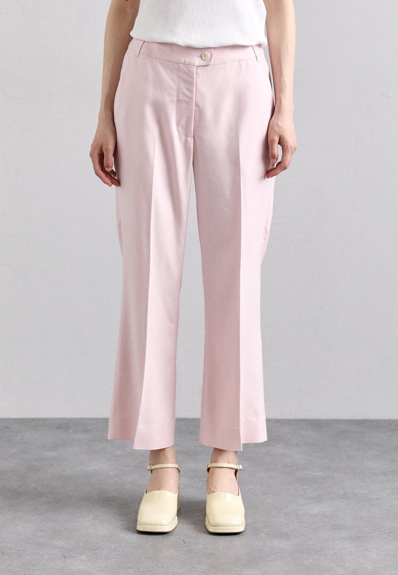 Personne portant un pantalon court rose clair avec un bouton à l'avant et des chaussures crème à bout carré avec des brides à la cheville.