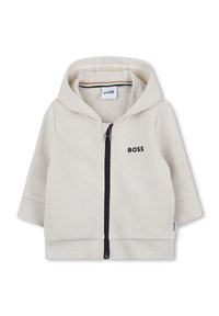 Veste à capuche zippée en mélange de coton beige clair. Elle comporte une fermeture éclair sur le devant, un ourlet côtelé et un logo subtil en noir.