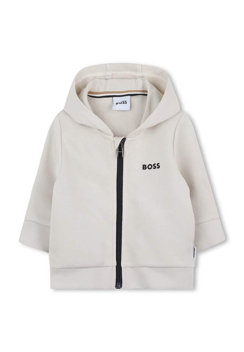 Veste à capuche zippée en mélange de coton beige clair. Elle comporte une fermeture éclair sur le devant, un ourlet côtelé et un logo subtil en noir.