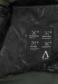 Sort stofmærke på jakken, der viser vandtæt 10.000 mm, åndbar 10.000 g/m²/24 timer, PFC-fri vandafvisende og vindafvisende egenskaber.