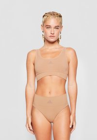 Nude sportinis liemenukas ir aukšto liemens kelnaitės rinkinys, pagamintas iš lygios, tamprios medžiagos. Yra Adidas logotipas ir paprastas, besiūlis dizainas.