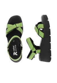 Sandales en cuir vert avec une semelle compensée, un design à brides croisées, une bride de cheville réglable et un coussin noir au niveau du pied.