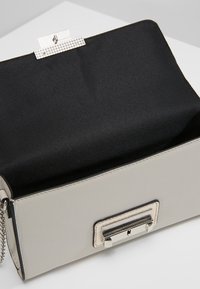 Světlostraková obdélníková kabelka s texturovaným povrchem, černým interiérem, magnetickým uzavíráním a stříbrným kováním na přední straně.