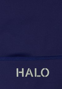Marineblauwe stof met zichtbare stiksels boven witte hoofdletters die "HALO" op het materiaal spellen.