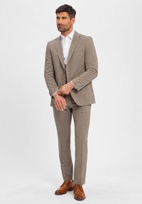 Jasnobrązowy garnitur w kratę o dopasowanym kroju, z dwoma guzikami w marynarce i slim fit spodniami. Uzupełniony białą koszulą i brązowymi butami.