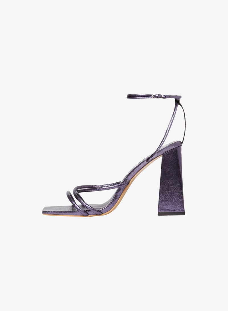 Sandales à talons hauts métalliques violettes avec un talon block, bouts ouverts et plusieurs fines lanières. Texture de surface lisse, design minimaliste.