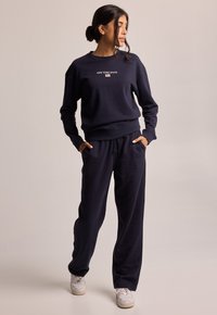 Felpa unisex blu navy e pantaloni jogger in morbido tessuto. Presenta la scritta "NEW YORK STATE", vestibilità comoda, polsini a costine e vita con cordino.