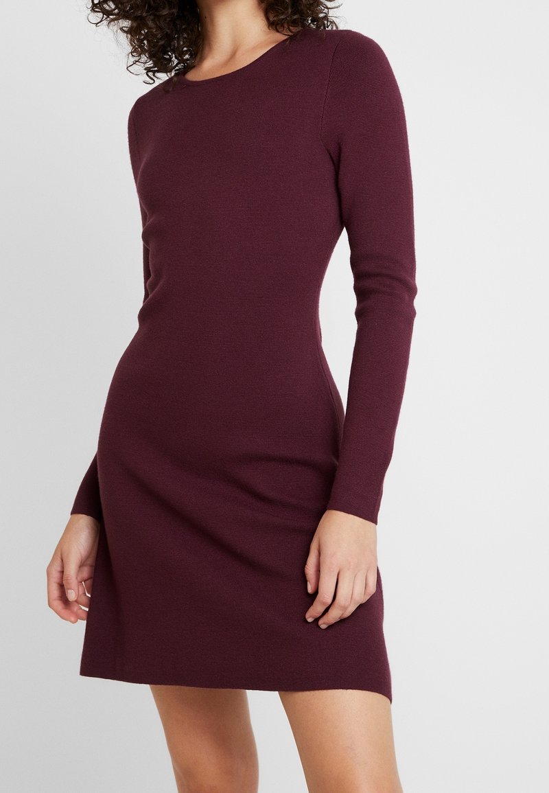 Robe bordeaux à manches longues en tissu côtelé, avec un col arrondi et une silhouette ajustée, s'étendant au-dessus du genou.