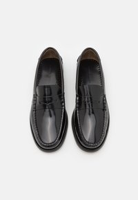 Mocassins en cuir noir avec une finition brillante, présentant un design de mocassin cousu et un accent de nœud décoratif à l'avant.