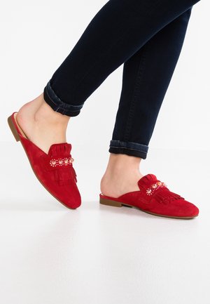 Røde ruskindsmules med frynser og perleudsmykning, med lav profil og flad sål, båret med mørke jeans.