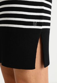 Falda de punto a rayas blancas y negras con una abertura lateral, que presenta un pequeño logo cerca del dobladillo. Textura suave y diseño ajustado.