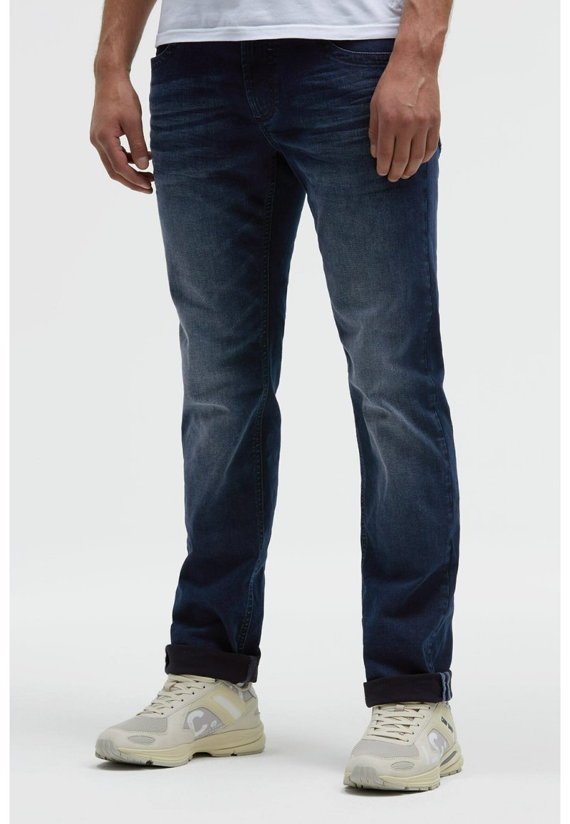 Dunkelblaue Jeans aus Denim mit geradem Schnitt und leichter Verblassung, ausgestattet mit klassischem Fünf-Taschen-Design und hochgekrempelten Bündchen. Kombiniert mit hellen Sneakern.